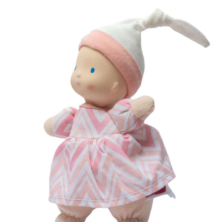 Baby doll in a pink and white chevron dress with a matching hat on a white background.