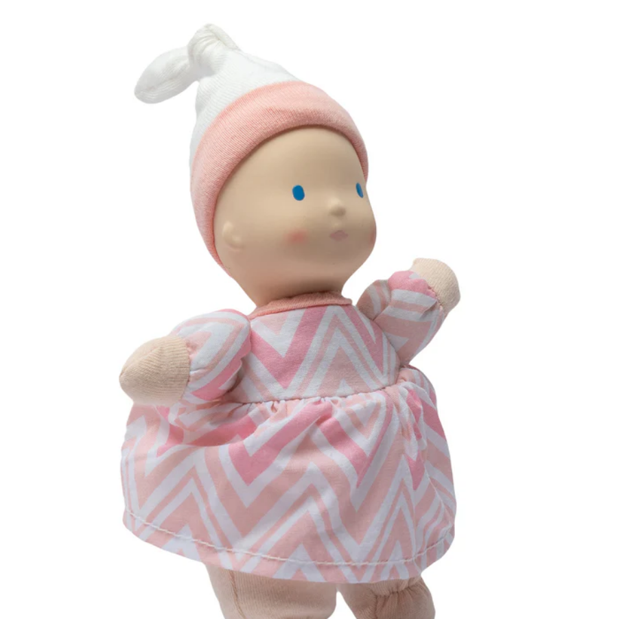 Baby doll in a pink and white chevron dress with matching hat on a white background