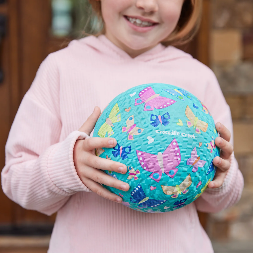 Child holding a blue butterfly-patterned ball with 'Crocodile Creek' branding.