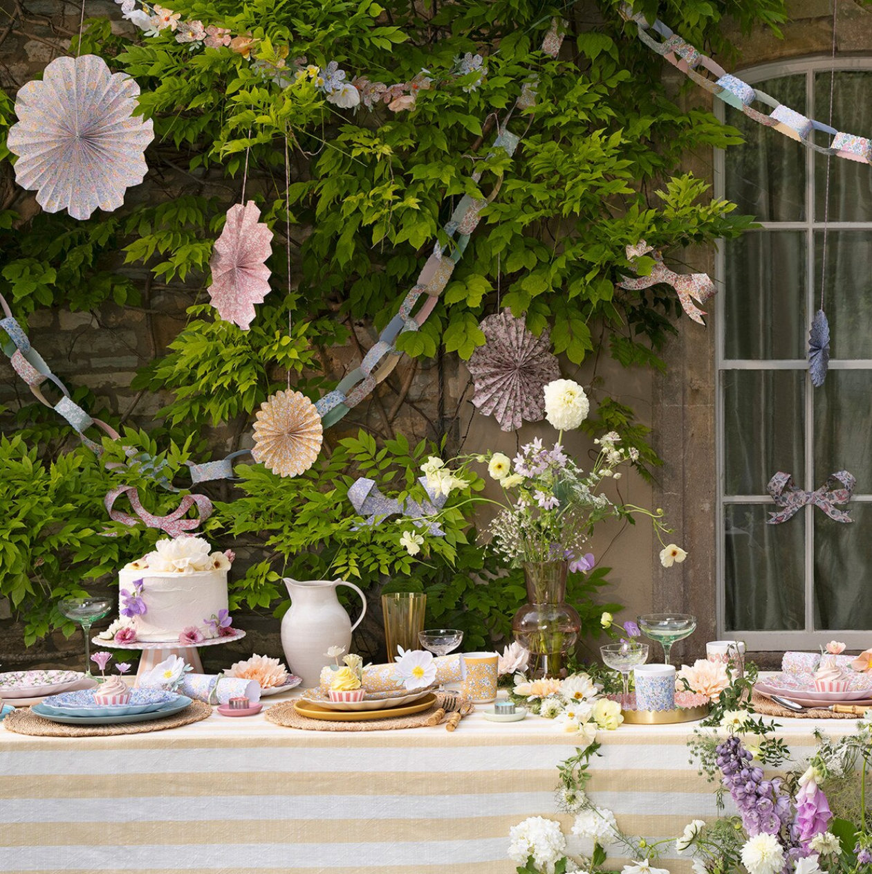 Decorative outdoor setting with flowers, tableware, and a cake.