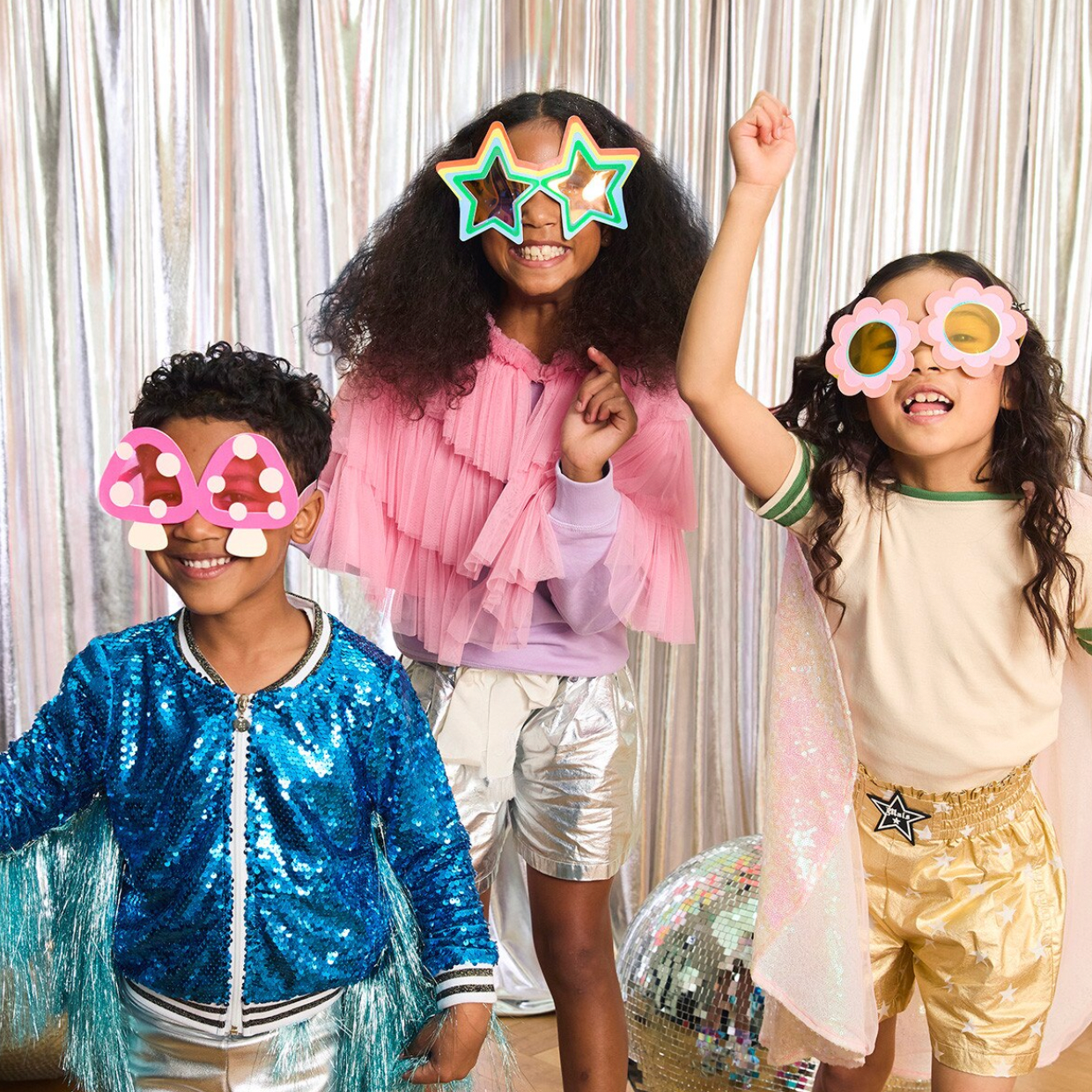 Three children wearing colorful props in front of a silver curtain