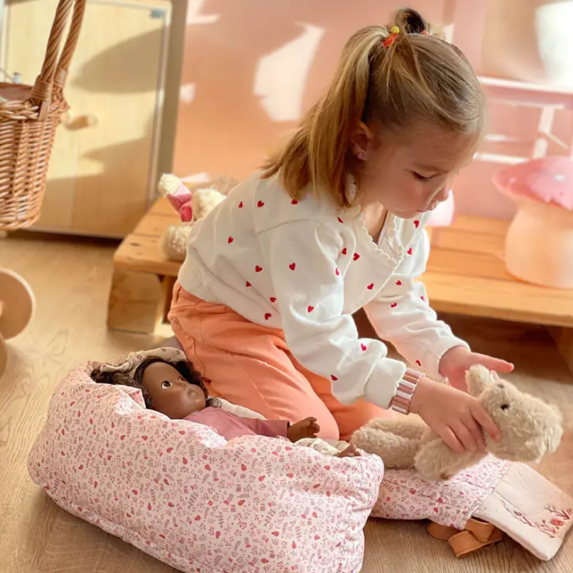 Child playing with dolls and a plush toy on a wooden floor.