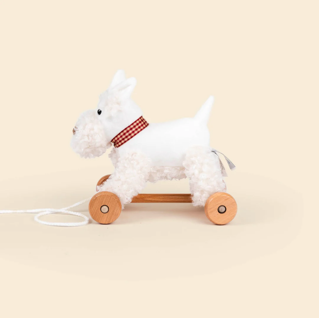 White plush dog toy with wooden wheels on a beige background