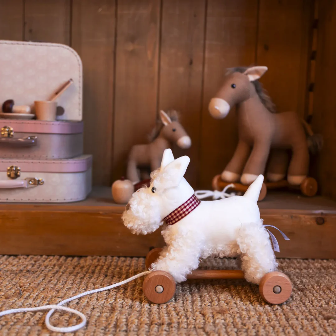 White dog toy on wheels with a red ribbon, surrounded by other toys in the background.