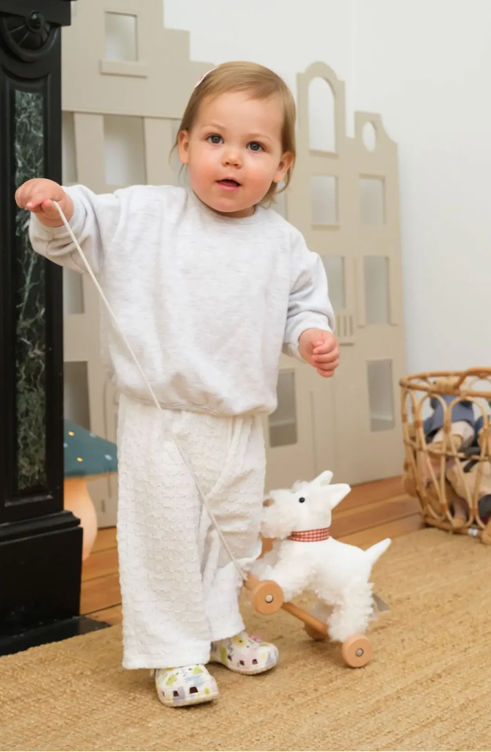 Child in a white outfit playing with a toy horse indoors.
