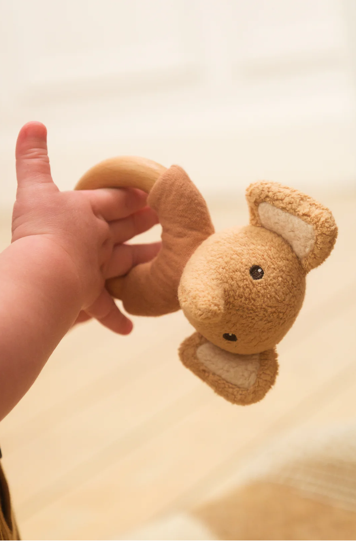 Hand holding a small brown plush toy against a light background