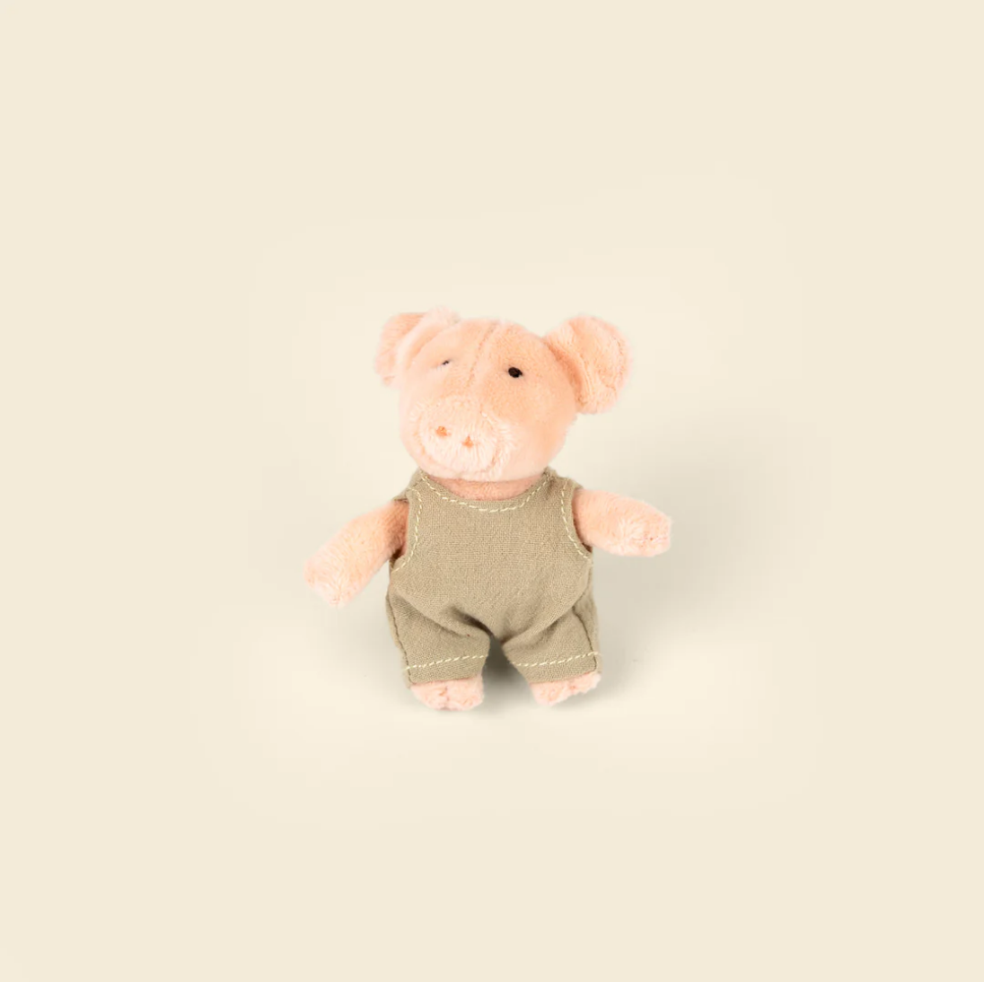 Stuffed toy pig wearing green overalls on a beige background