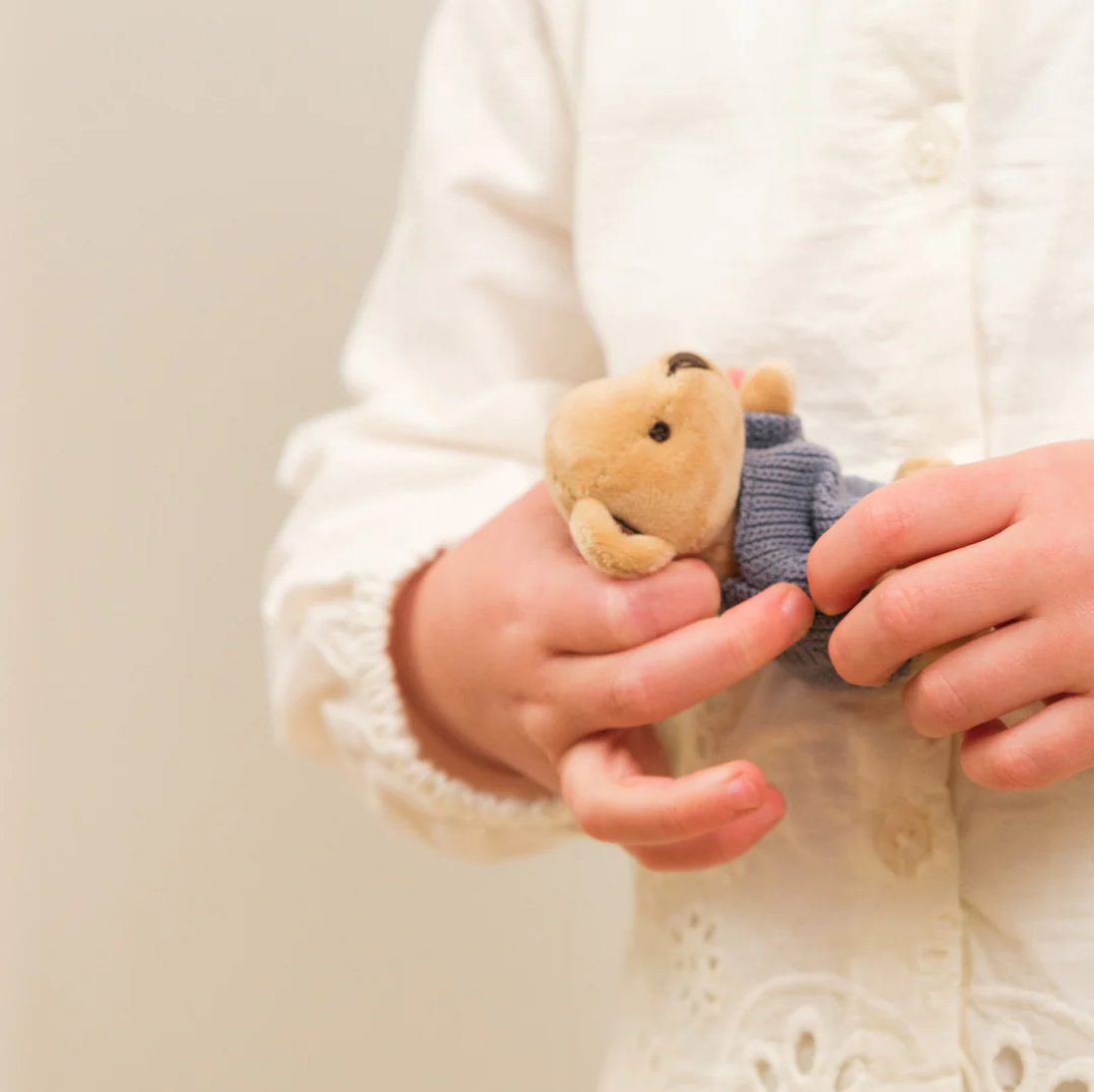 Small teddy bear toy held by a child wearing a white sweater.