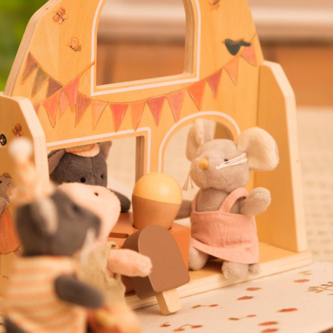 Toy mouse with a pink dress standing in front of a wooden letter 'H' with decorative elements.