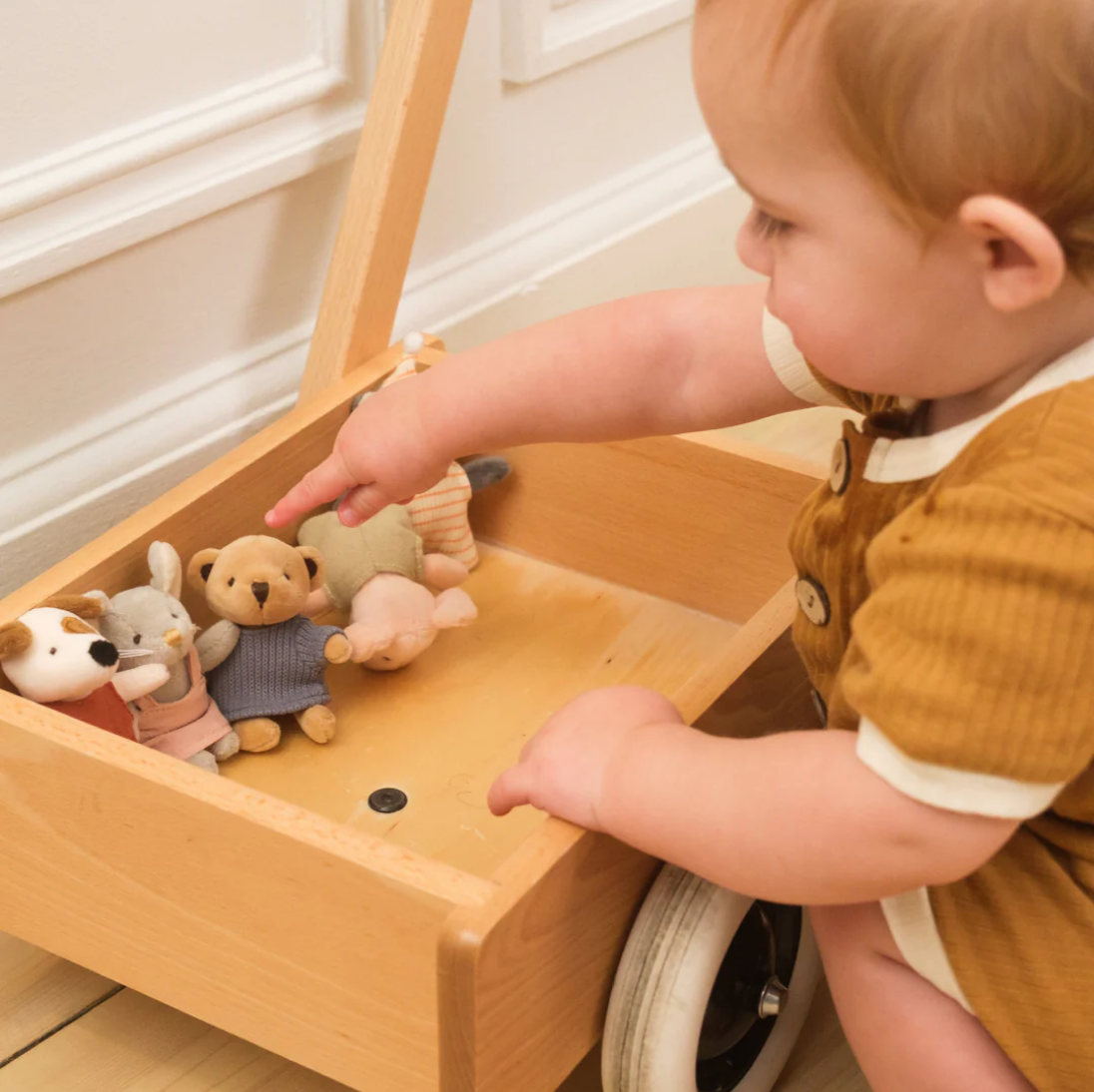 Child playing with plush toys in a wooden toy box.
