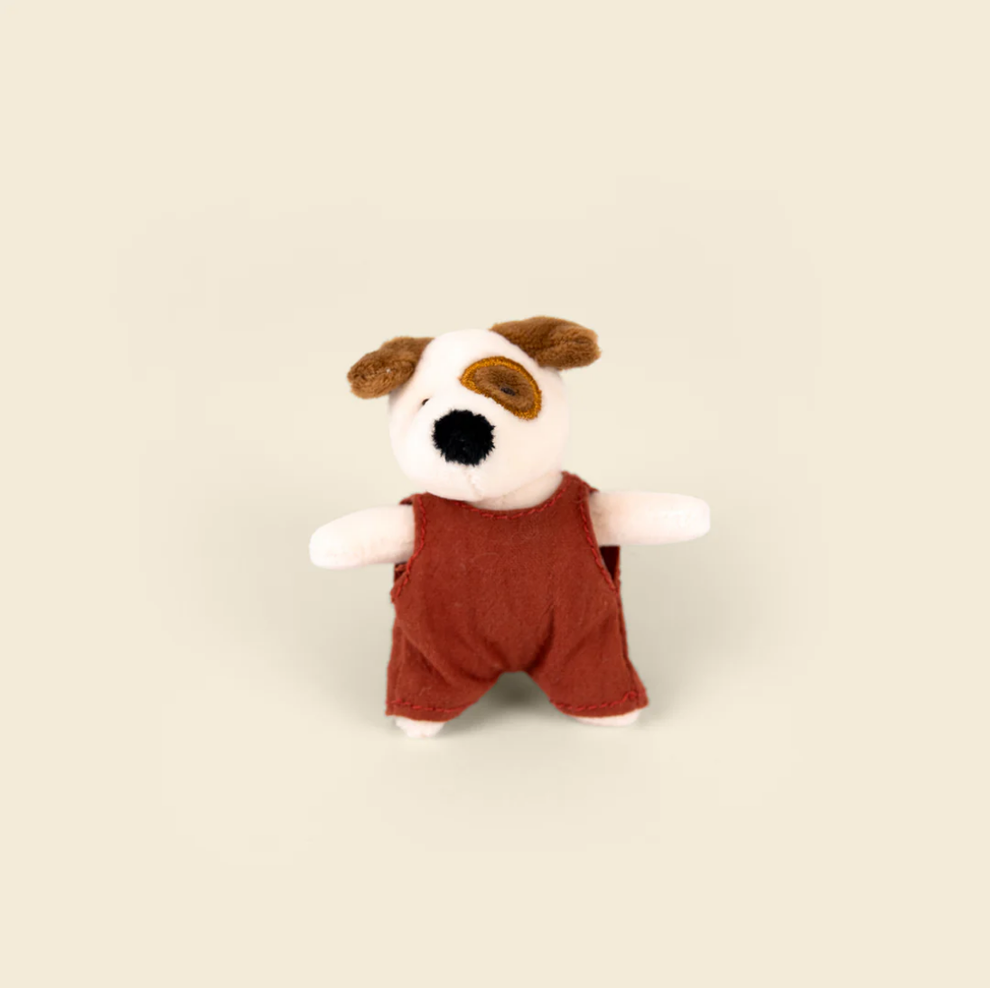Stuffed toy dog wearing red overalls on a beige background