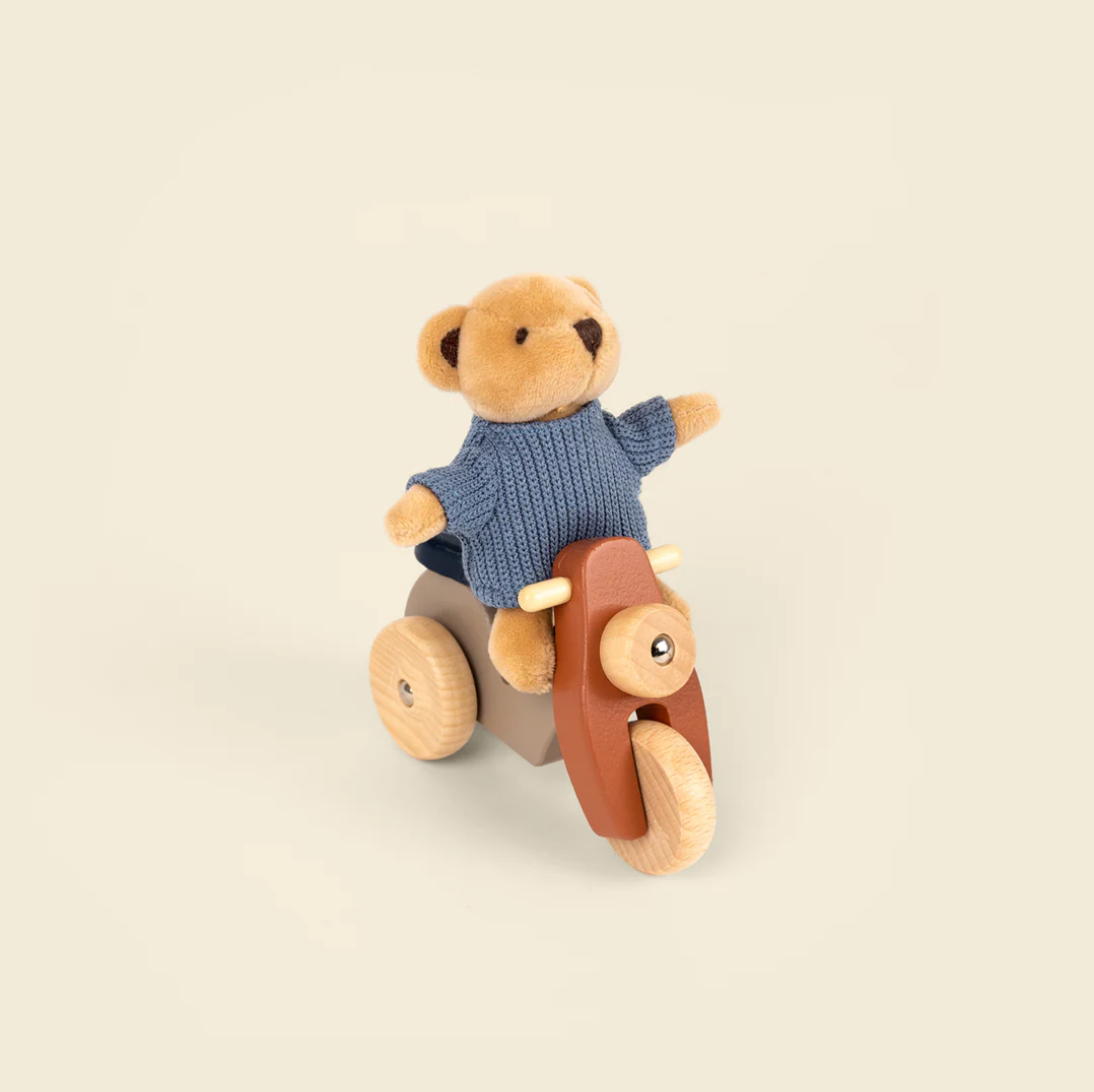Toy bear on a wooden bike with a blue sweater on a beige background