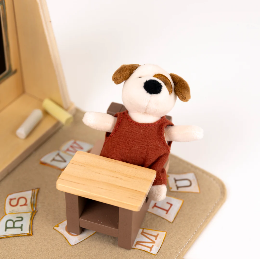 Stuffed dog toy at a desk with educational letters on a white background