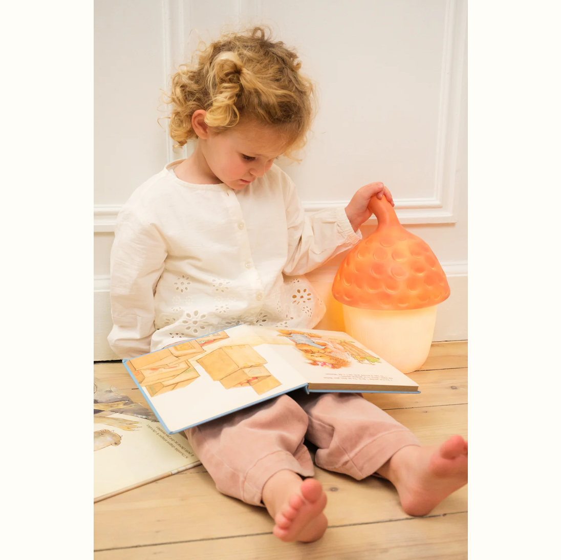 Child reading a book with a soft toy on a wooden floor.