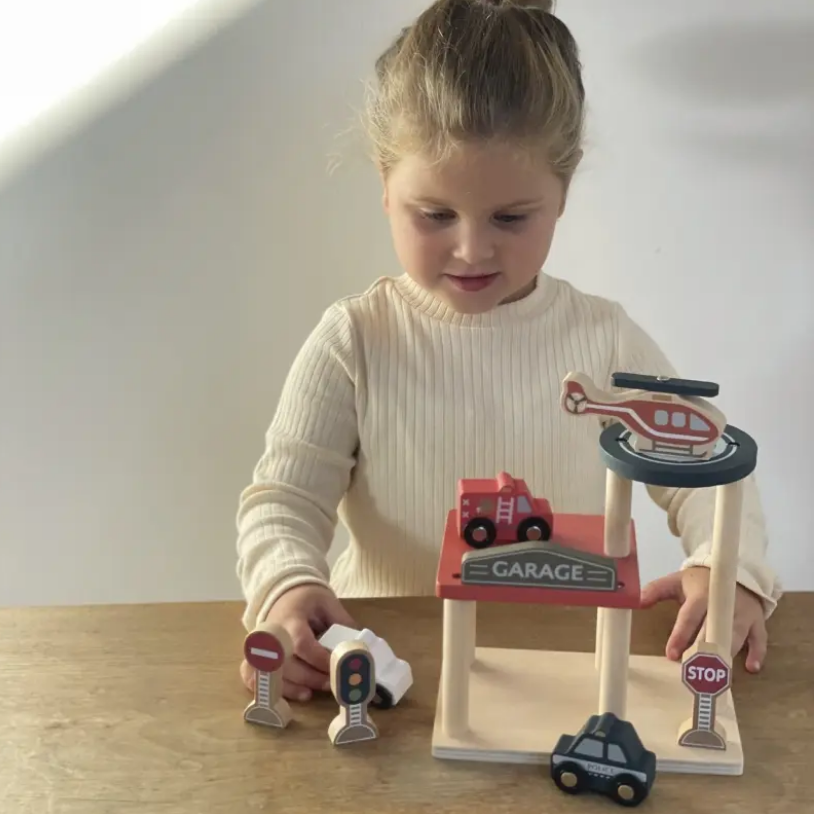 Child playing with a wooden toy garage set on a wooden table.