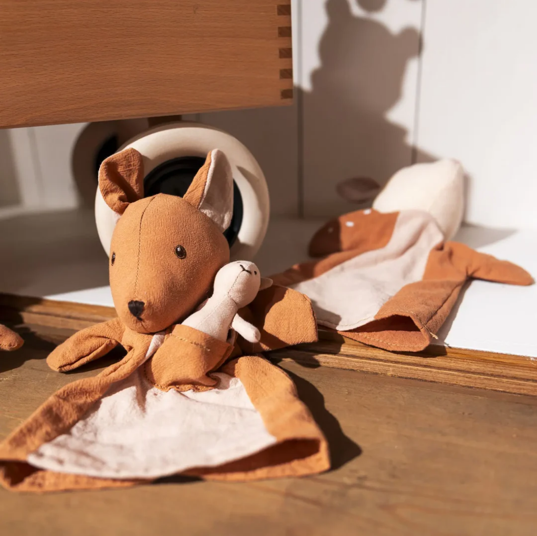 Brown plush toy resembling a kangaroo on a wooden surface with a white background