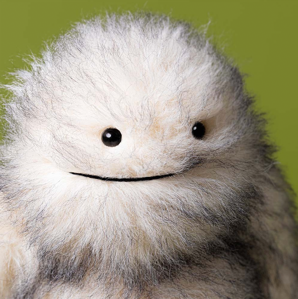 Close-up of a fluffy white creature with black eyes against a green background
