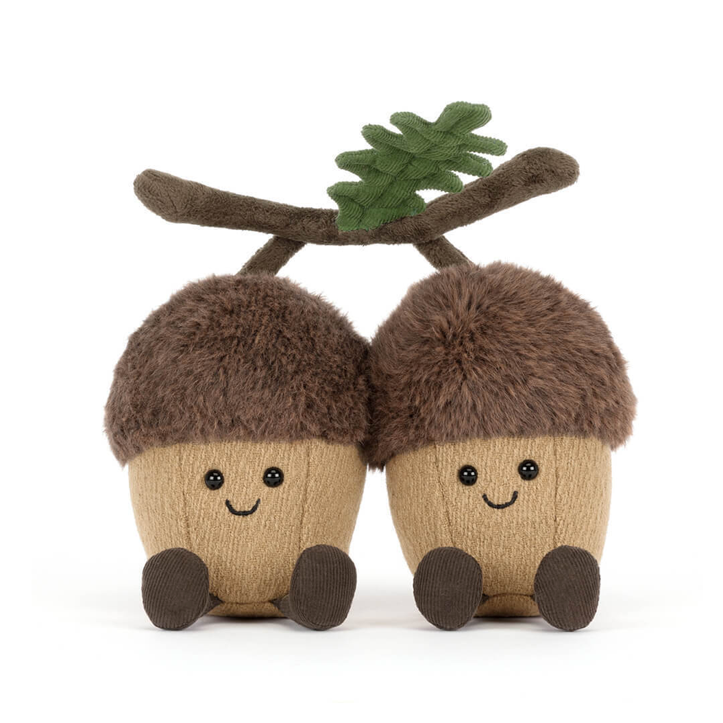Two plush acorns with faces and a twig with leaves on a white background