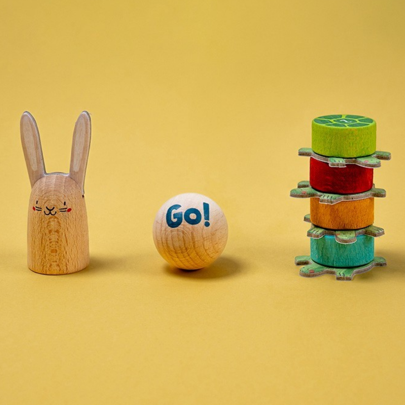 Wooden toy rabbit, ball with 'Go!' text, and colorful tower on a yellow background