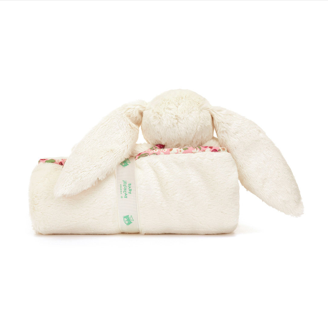 A plush cream bunny blanket with long floppy ears and a small floral patterned lining peeking out, shown on a white background 