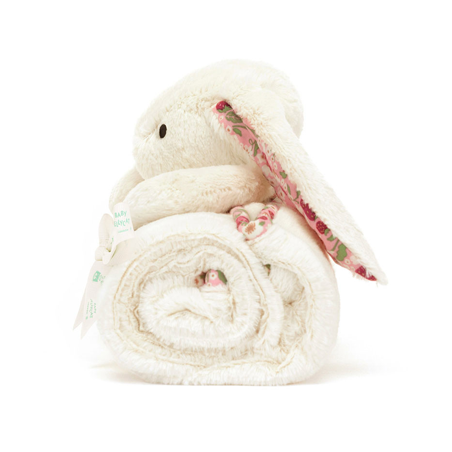 A plush bunny-shaped blanket or towel in a warm cream/off-white color, rolled into a spiral shape with a long floppy ear showing a pink floral pattern. The item is photographed on a plain white background 