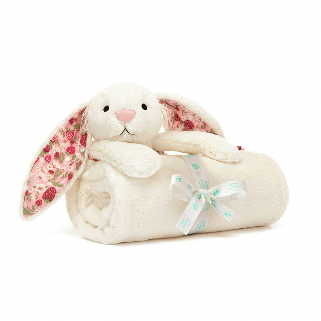 A plush cream bunny blanket with floral-patterned ears and a pale blue ribbon tied around a rolled cream throw, shown on a white background 