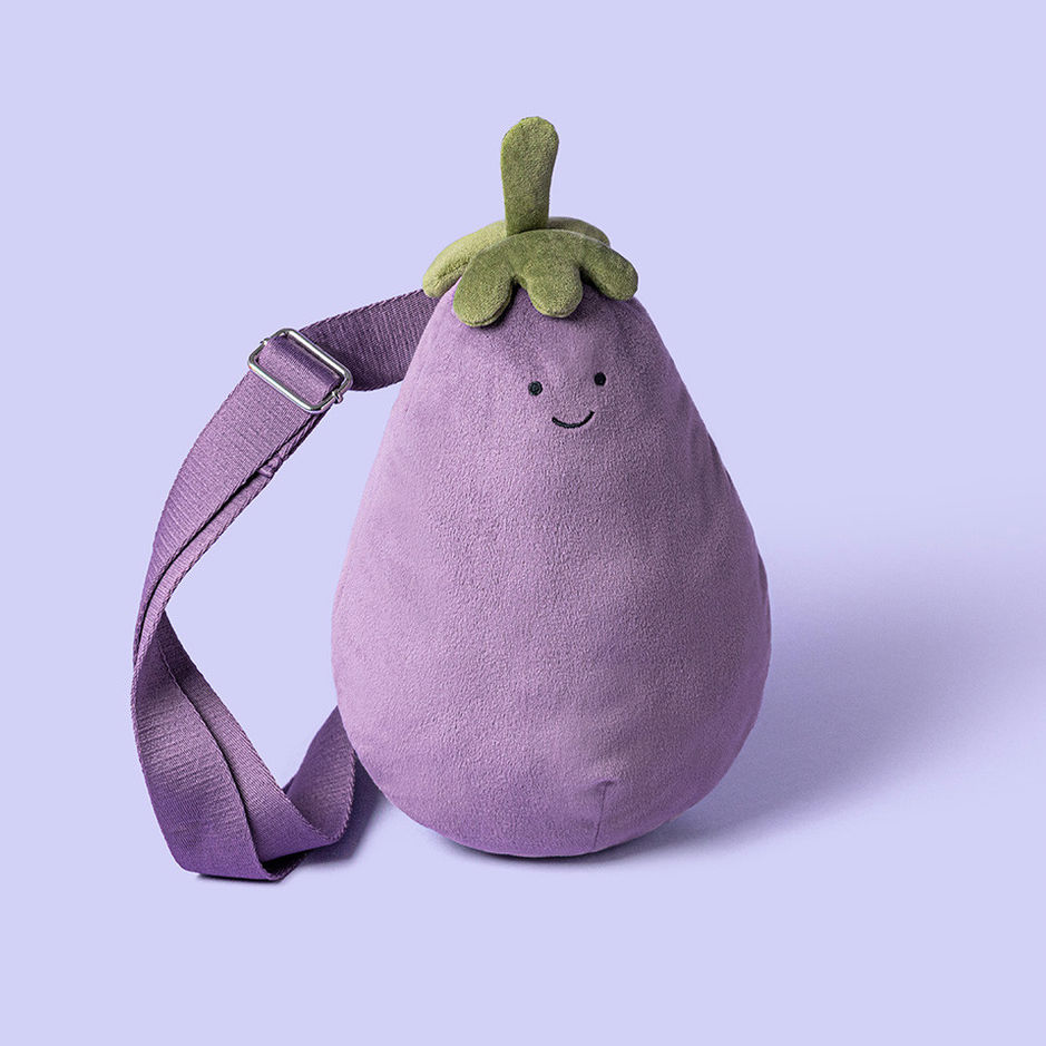 A purple eggplant-shaped shoulder bag with a green stem and embroidered face, shown on a light lavender background.