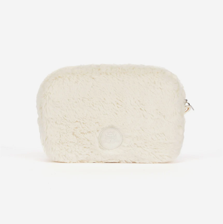 A cream-colored faux fur cosmetic pouch with a circular embossed logo on the front and a silver zipper pull on the side, set against a plain white background.