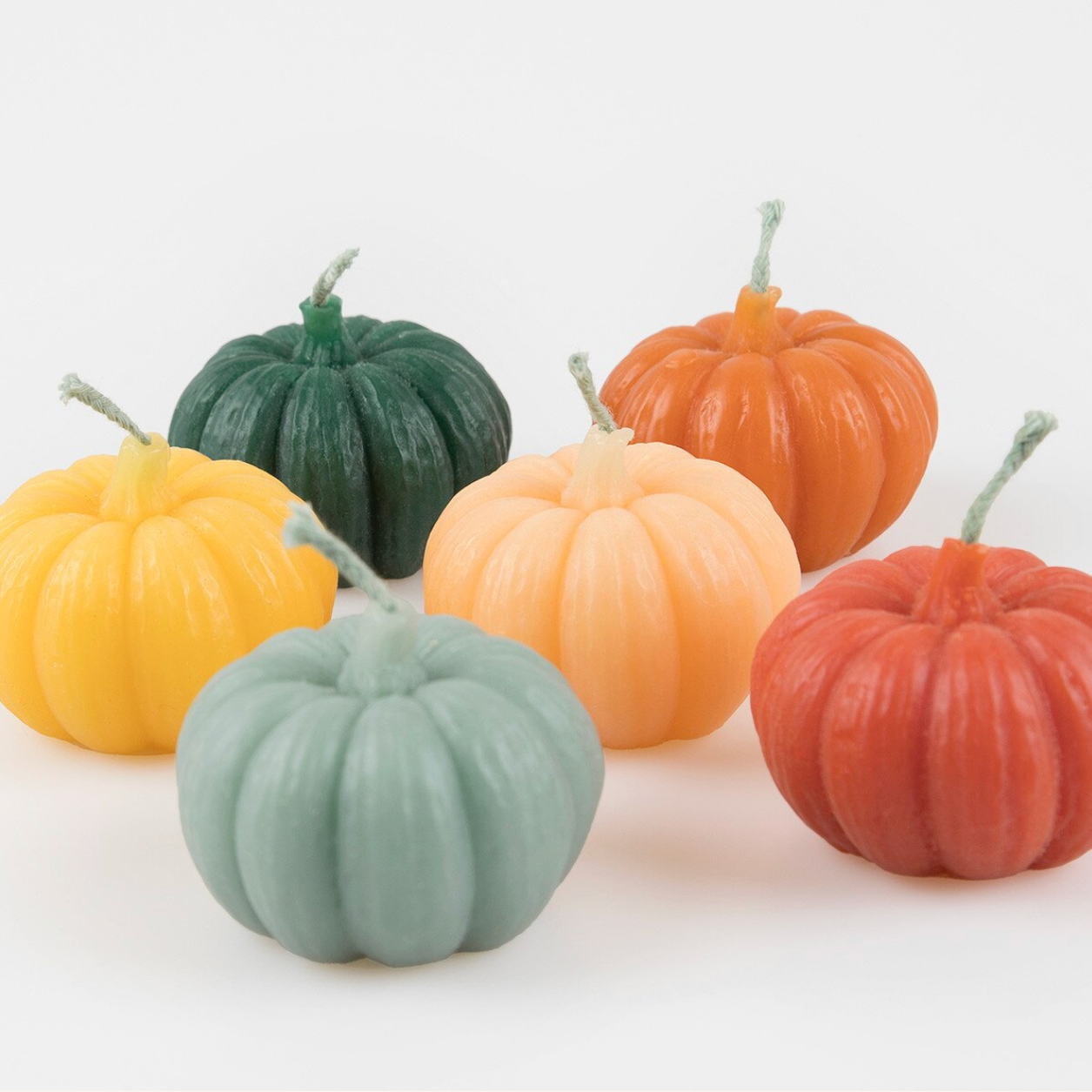 Six small decorative pumpkin-shaped candles in assorted fall colors, including dark green, orange, yellow, peach, rust red, and pale mint, arranged on a white background.