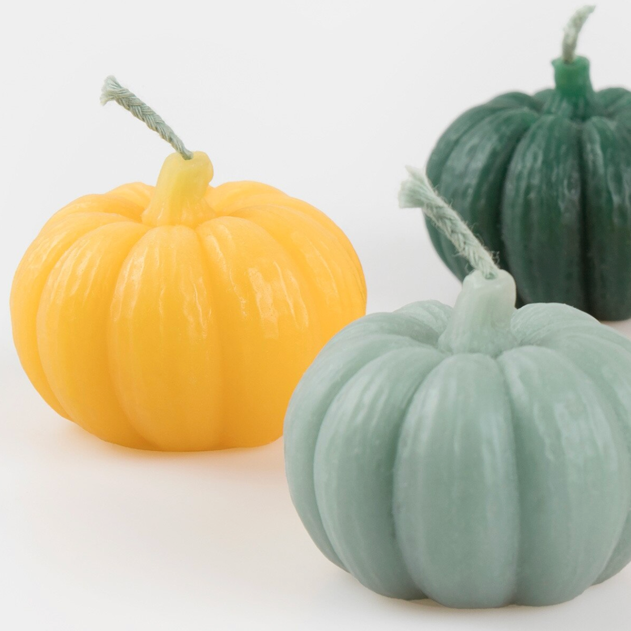 Three pumpkin-shaped candles with faux stems, shown in yellow, sage green, and dark green on a white background.