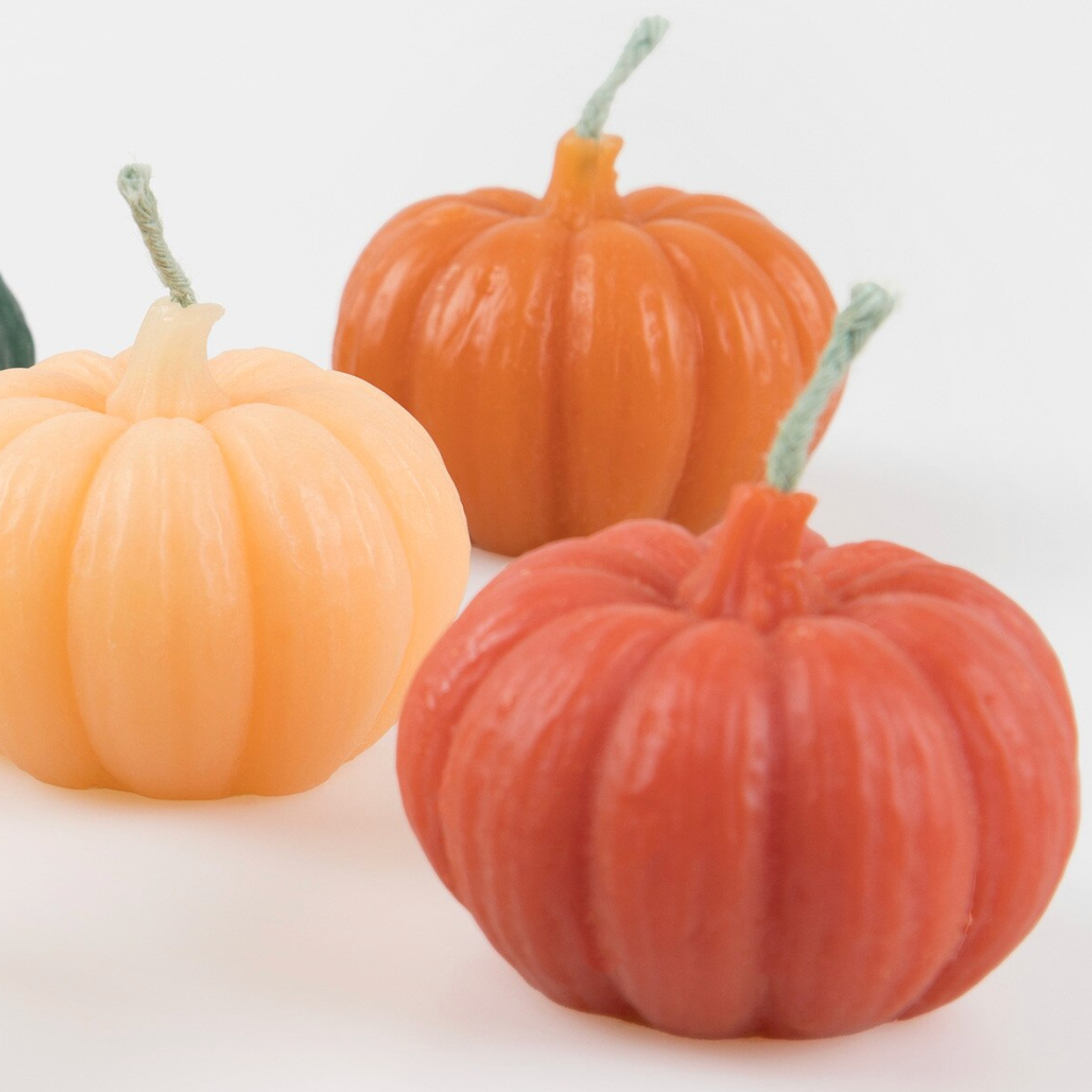 Three pumpkin-shaped candles in shades of peach, orange, and terracotta, arranged on a white background.