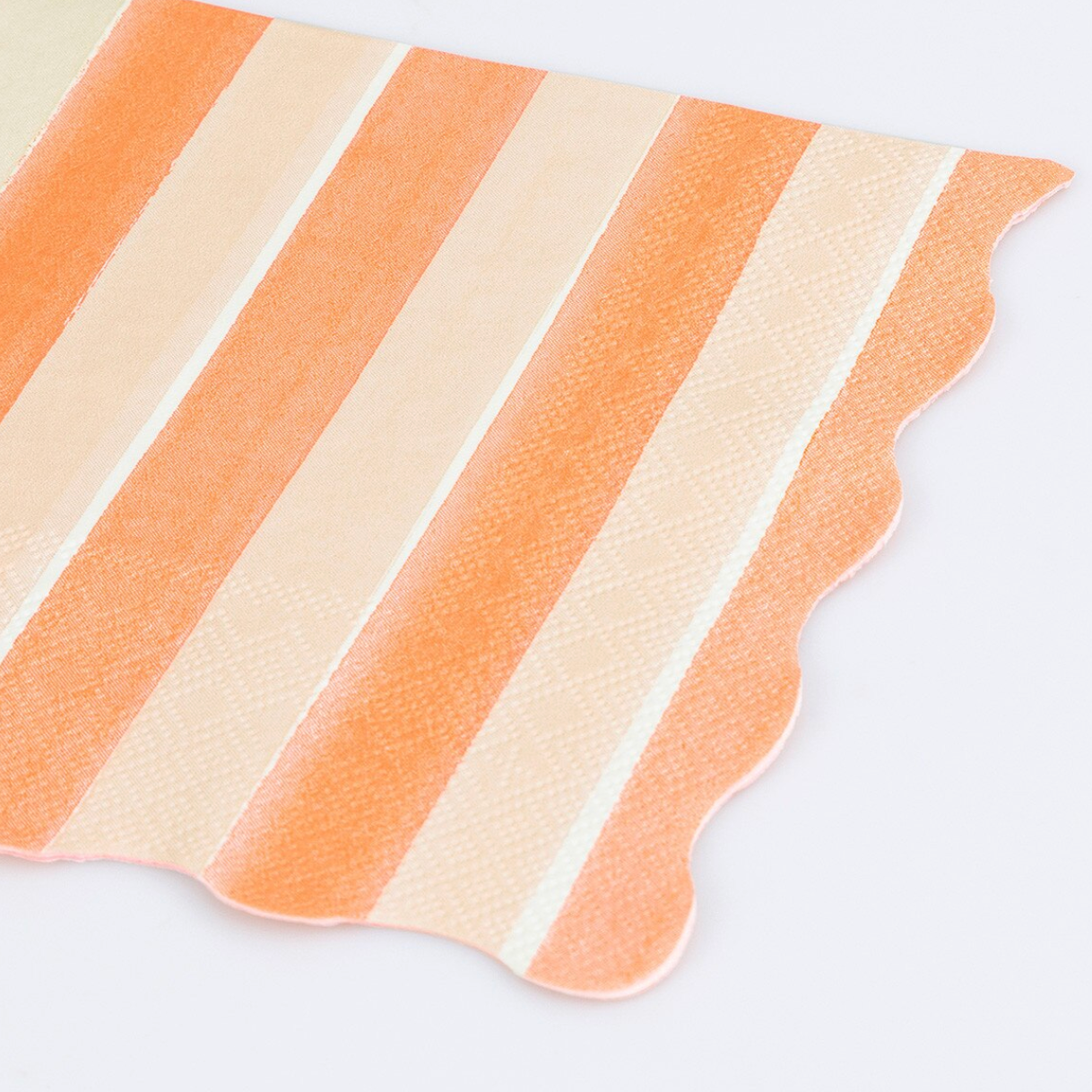 A close-up of a striped napkin with alternating peach, cream, and off-white vertical bands and a scalloped edge, shown on a light gray background.