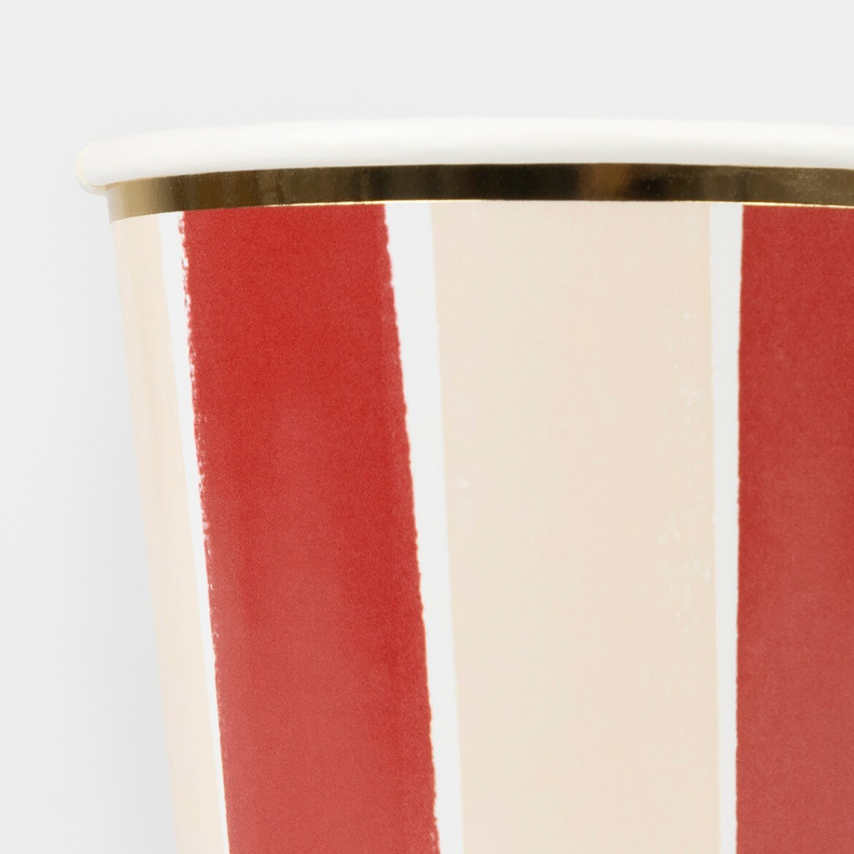 Close-up of a paper cup with vertical stripes in red and cream, featuring a metallic gold rim on a light gray background.
