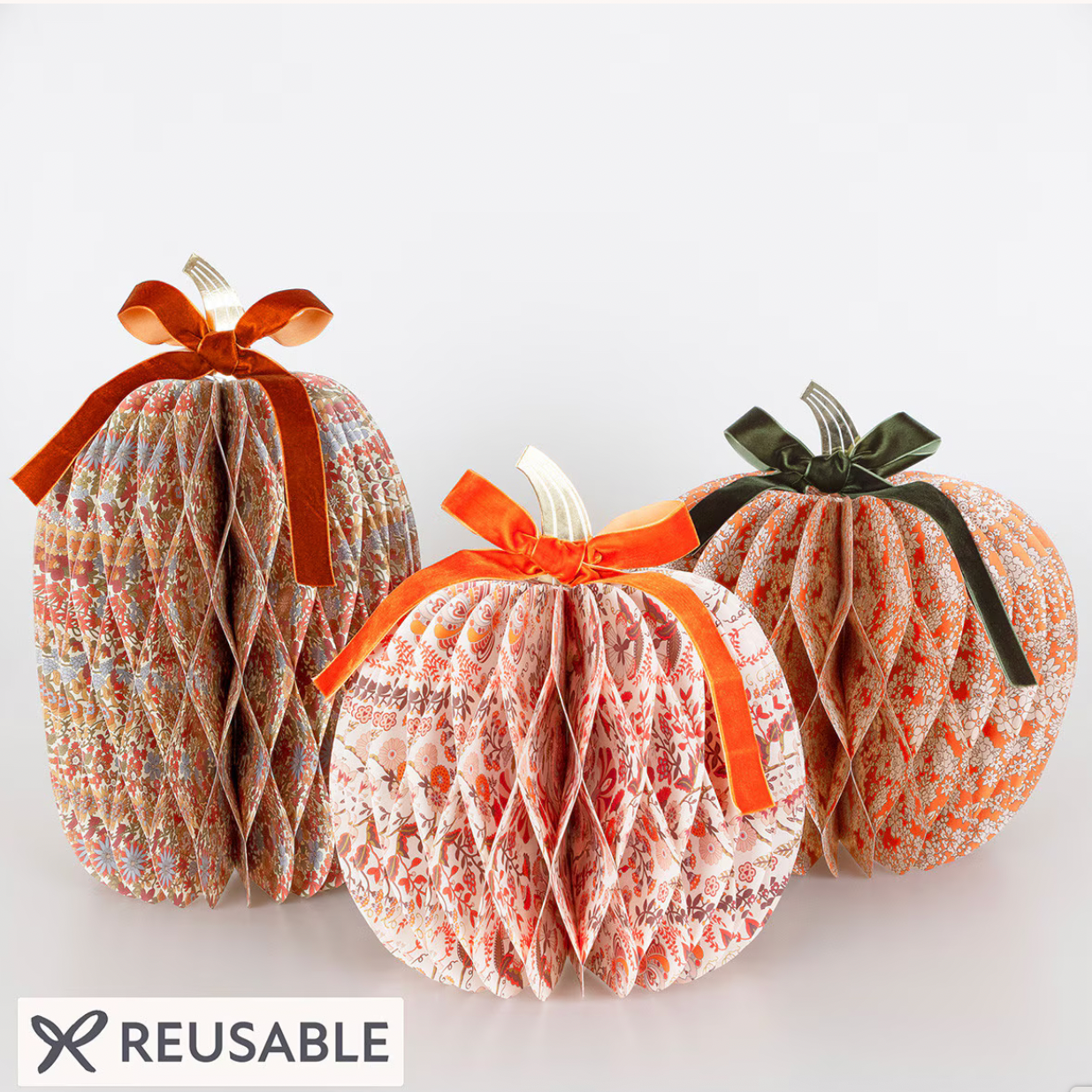 Three reusable paper pumpkin decorations with a printed autumn pattern, tied with orange and dark green ribbons, shown on a white background with a 'REUSABLE' label.