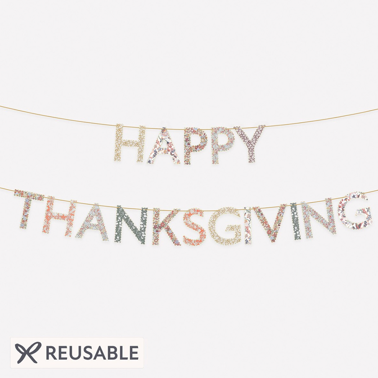 A reusable 'Happy Thanksgiving' letter banner made of glittery, metallic letters strung on thin cords against a plain light background, with a 'REUSABLE' badge at the bottom left.