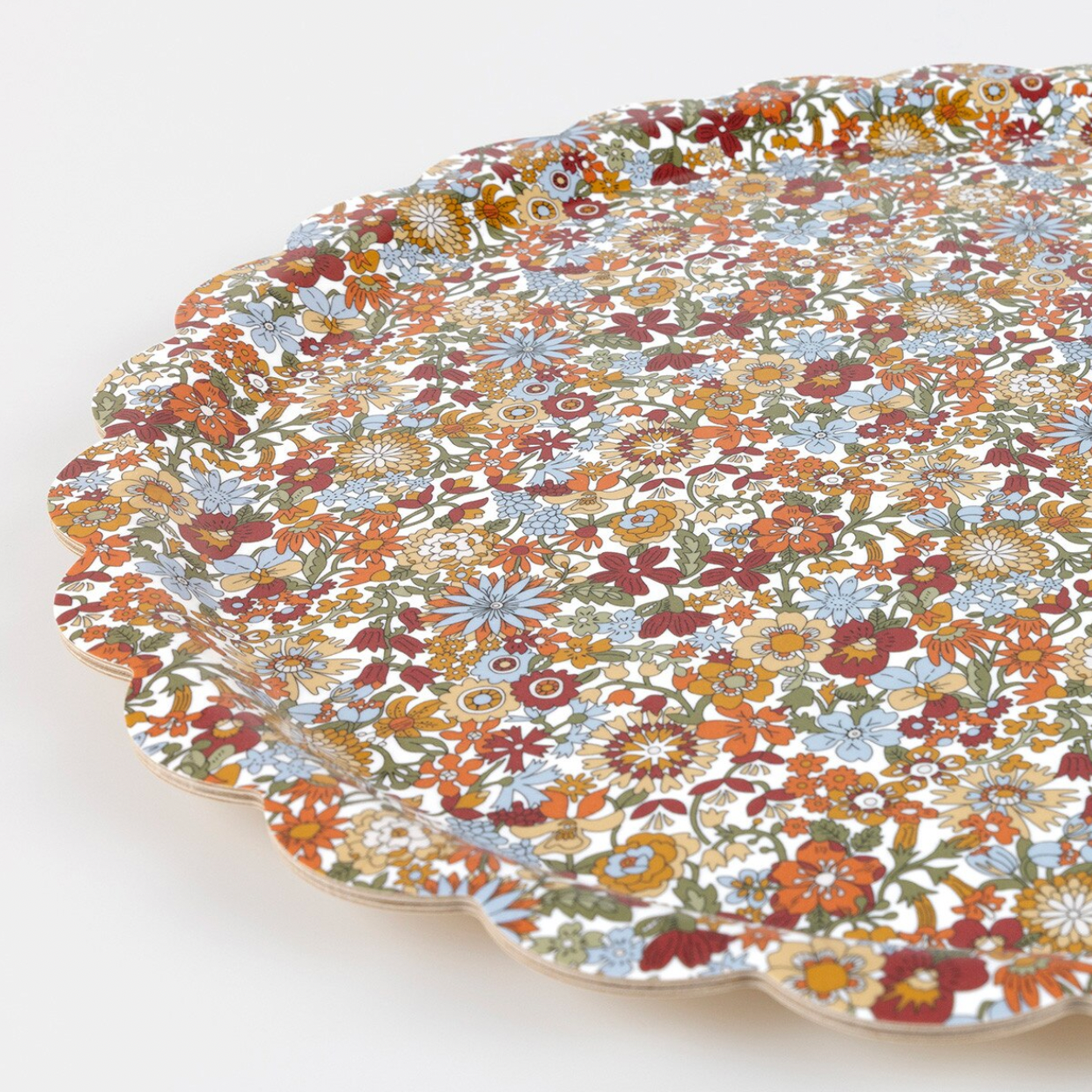 A scalloped ceramic serving platter with an all-over dense floral print in muted orange, red, blue, green, and cream tones, photographed on a plain white background.