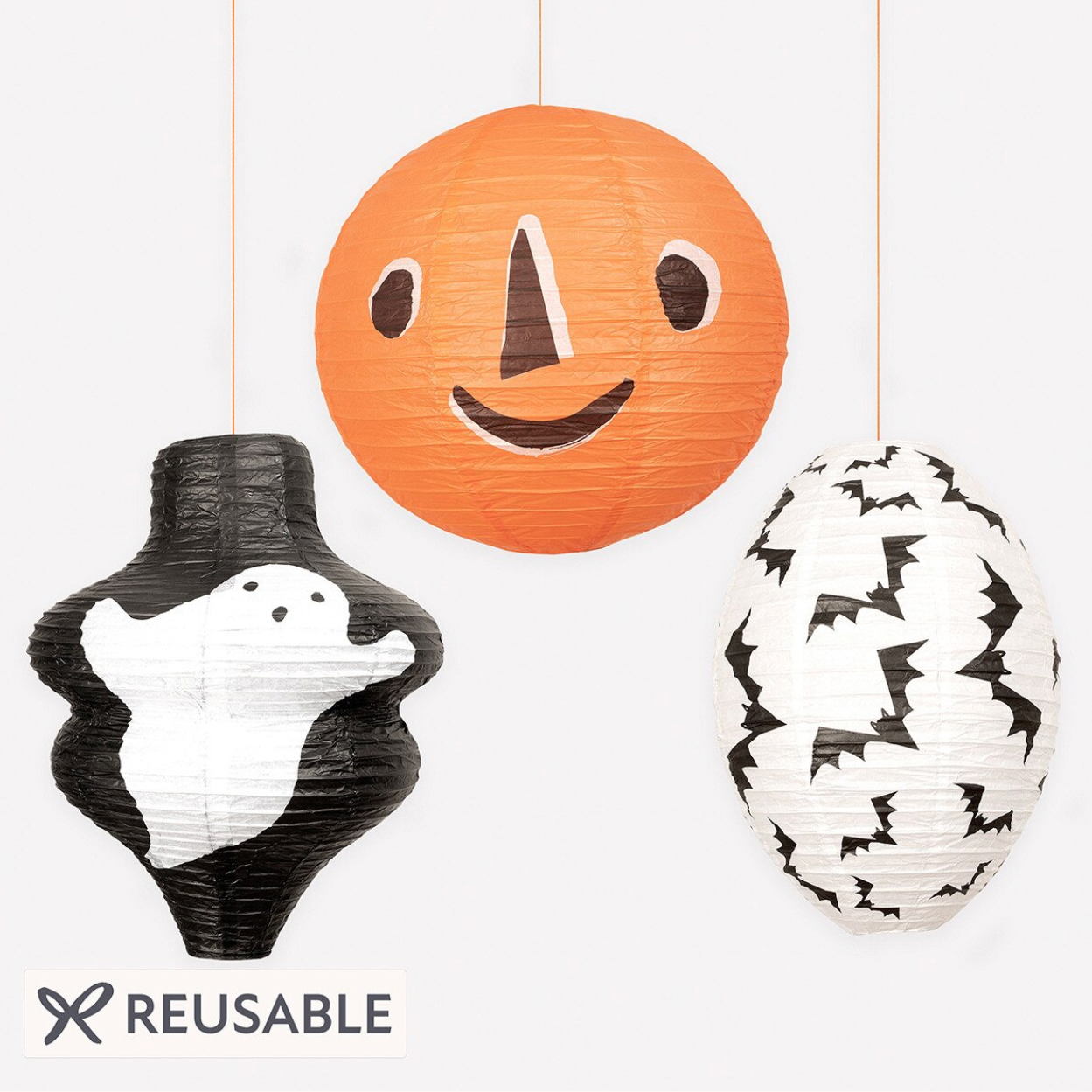 Three reusable hanging paper lanterns on a white background: an orange pumpkin lantern with a face, a black ghost lantern, and a white egg lantern with black bats. The word REUSABLE appears below.