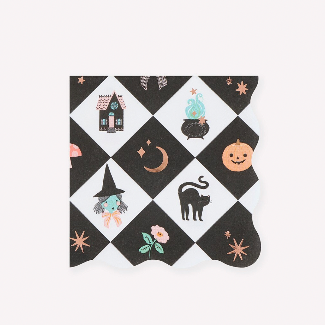 A single napkin with a Halloween-themed black and white diamond pattern, featuring illustrations of a witch's house, cauldron, moon, jack-o'-lantern, cat, and flowers, shown on a plain white background.