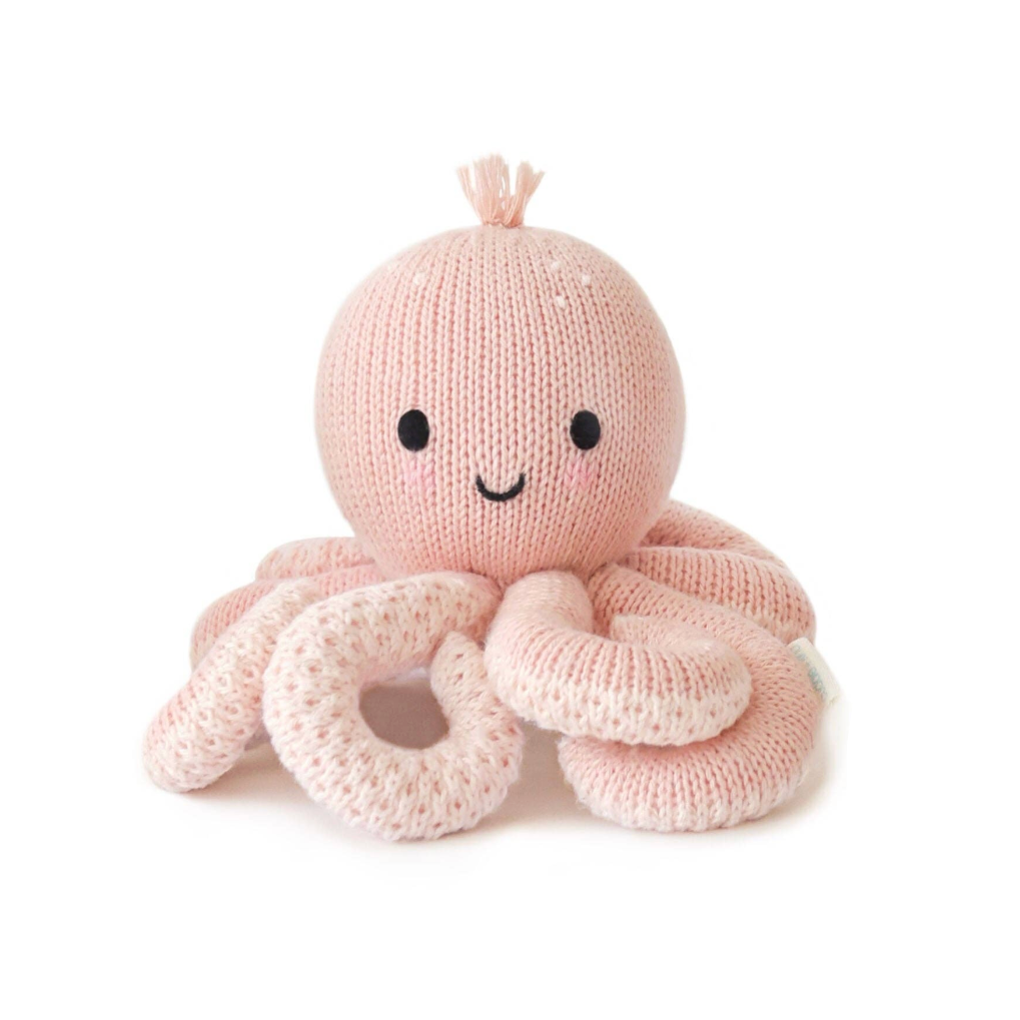 A knitted octopus plush toy in pale pink with black embroidered eyes and a curved smile, shown on a white background 