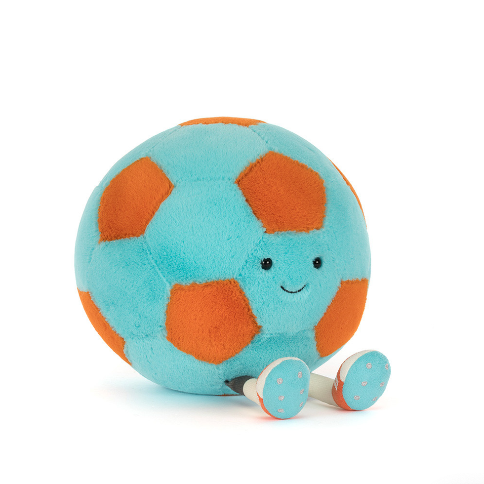 A small plush soccer ball toy with a light blue body, orange pentagonal panels, and a simple embroidered face, sitting on a white background.