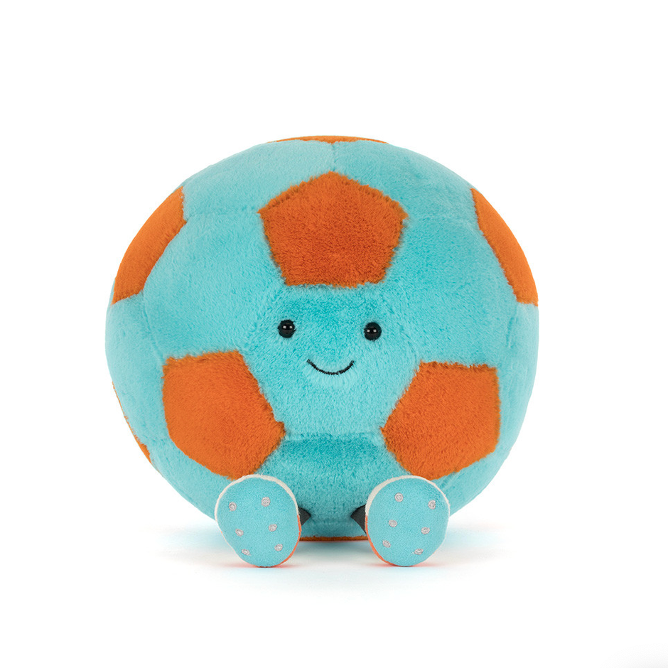 A plush jellycat soccer ball toy with a light blue body, orange pentagonal panels, and a small embroidered smiley face, shown on a white background