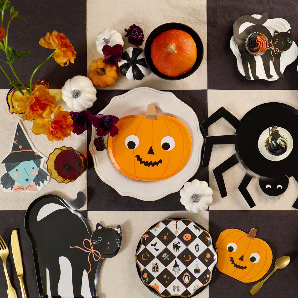 A styled Halloween table setting arranged in a checkered grid, featuring orange pumpkins, black cats, a spider plate, floral place settings, and gold cutlery on a dark and cream background.