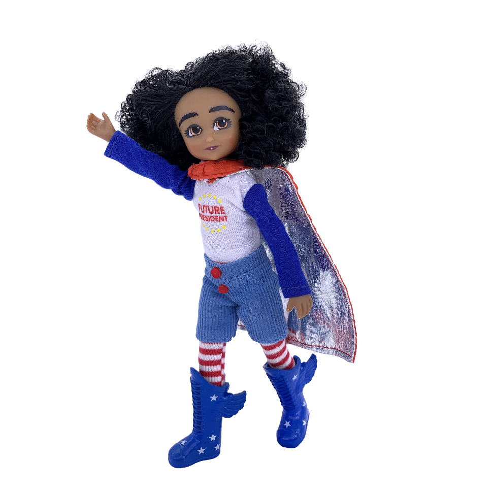A toy superhero doll with curly black hair, wearing a white shirt with red details, blue pants, red and white striped socks, blue boots, and a clear cape, shown on a white background.