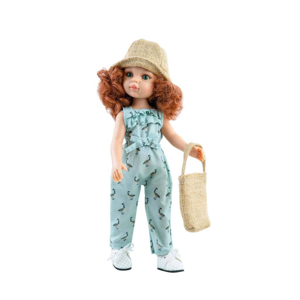 A doll with curly red hair wearing a beige hat, a light blue patterned romper, and white sneakers, holding a beige woven bag against a white background.
