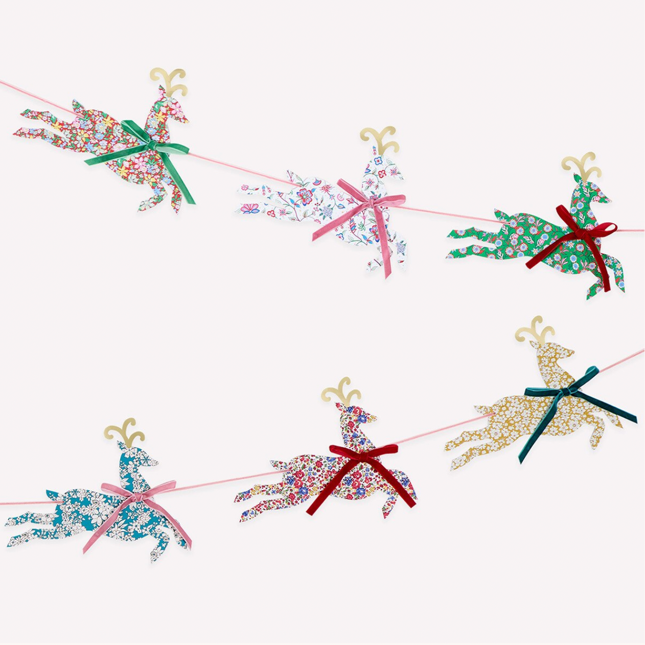 A festive Christmas garland featuring six reindeer cutouts, each filled with a different colorful floral pattern and tied to a thin pink string with red, green, pink, blue, red, and green ribbons.