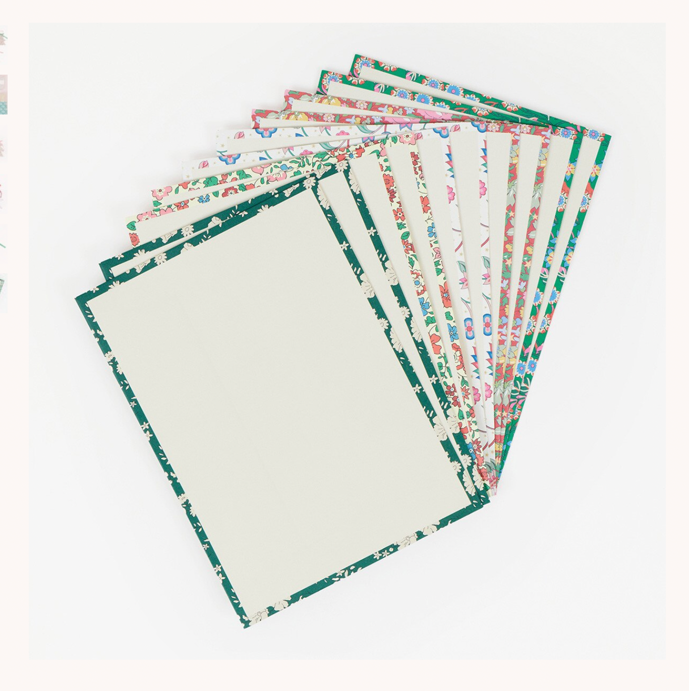 A fan of rectangular sheets with distressed dark green borders and multicolored floral patterns on the inner sides, arranged on a plain white background.