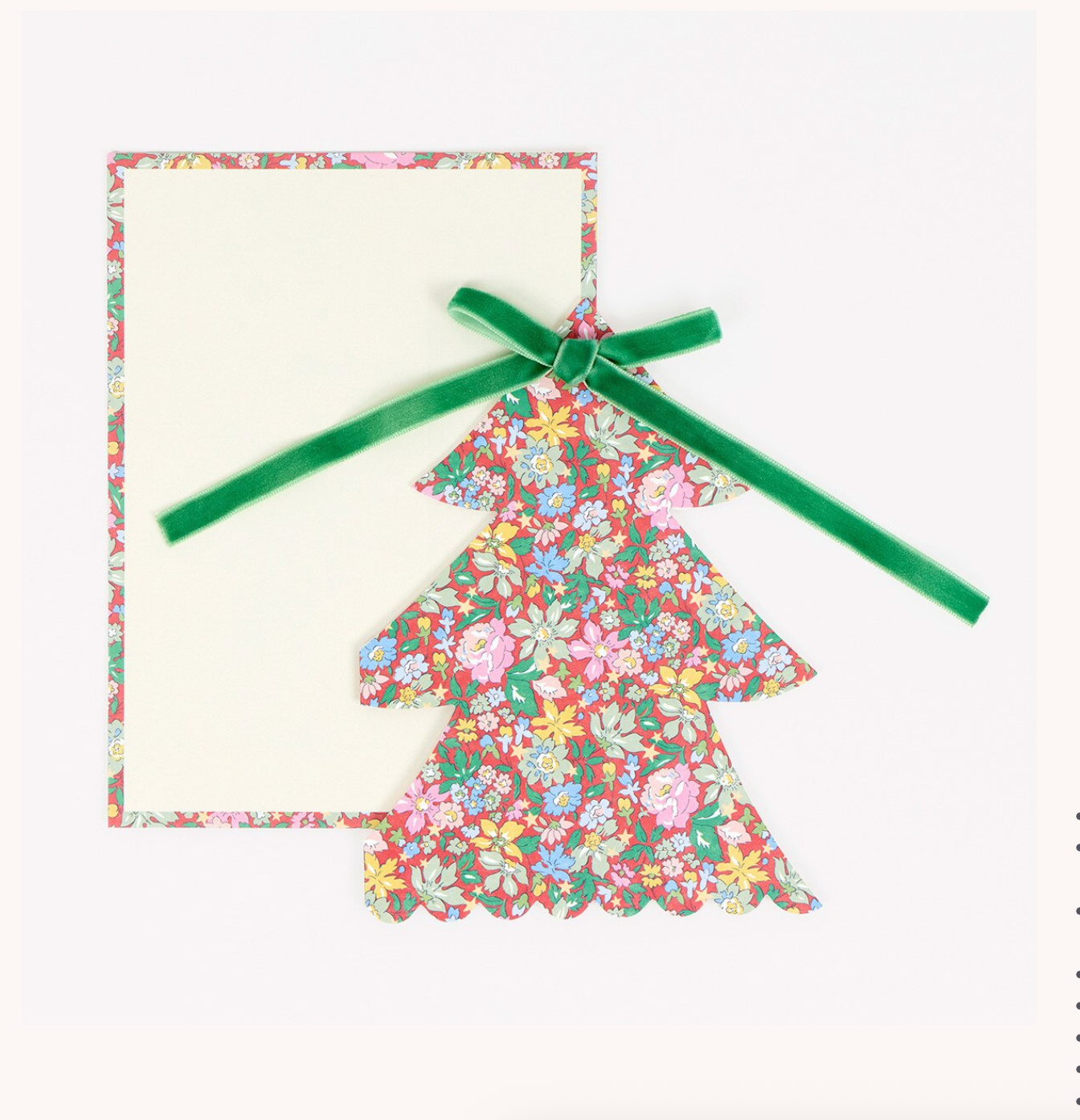 A Christmas-themed greeting card or envelope set featuring a scalloped floral tree shape with a green ribbon bow, placed in front of a matching floral-bordered blank card on a white background.