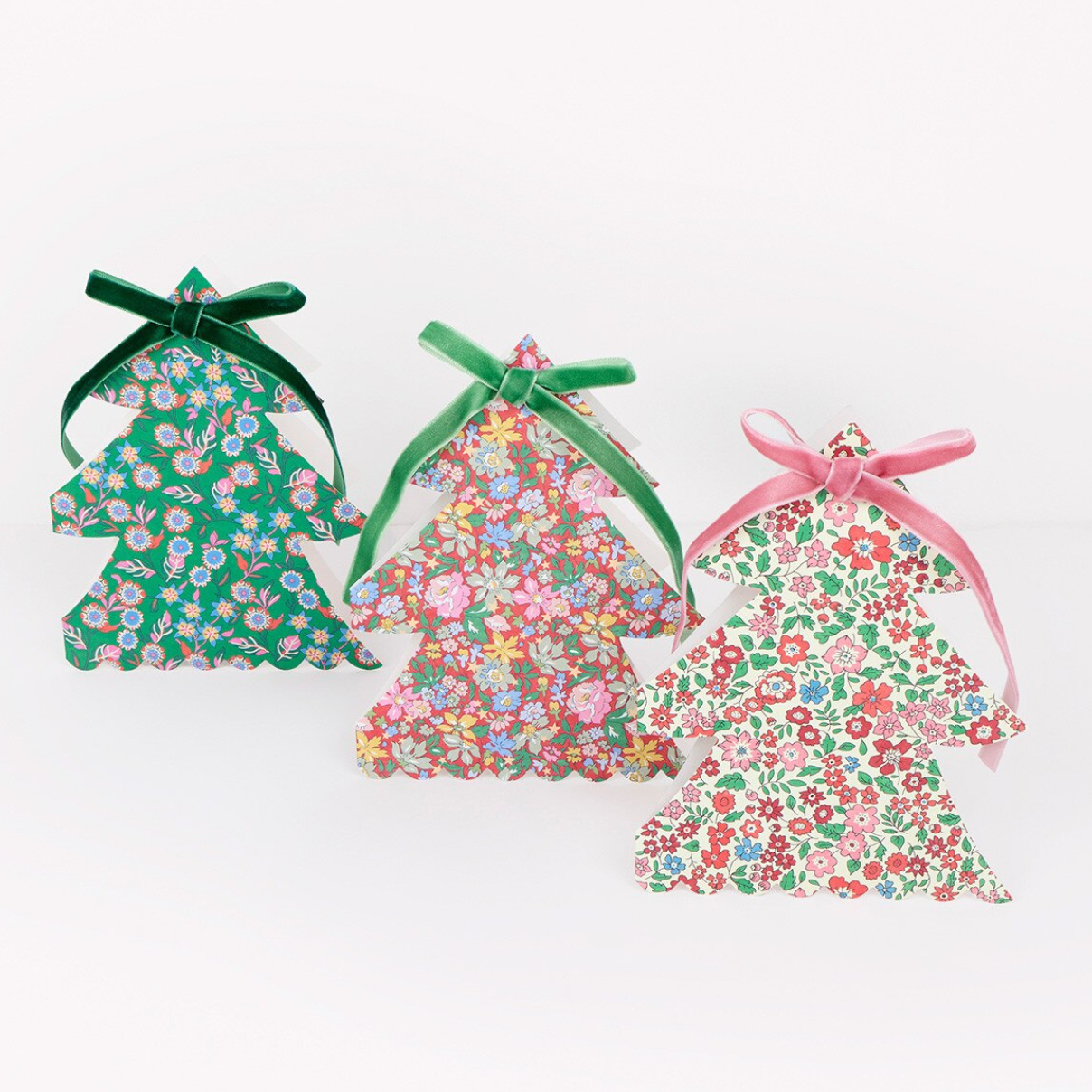 Three Christmas tree-shaped ornaments made from floral fabric, tied with green and pink ribbons, displayed on a white background.