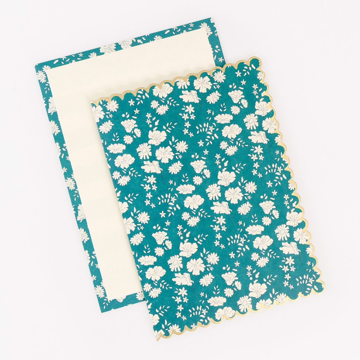 A teal and white floral patterned notebook or journal with a scalloped edge, shown with its cream-colored inner cover or page insert on a plain white background.