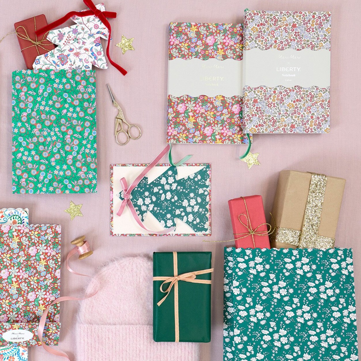 A flat lay of gift-wrapped notebooks and wrapped presents on a pale pink background, showing multiple floral and patterned paper wrap designs, ribbons, scissors, and kraft paper wrapping. A product sidebar is visible on the right edge.